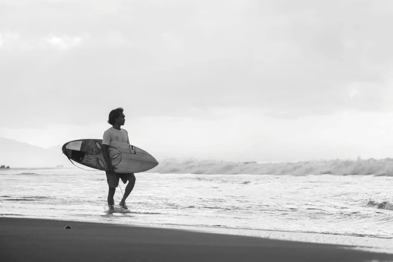 man walking into the ocean holding his surfboard