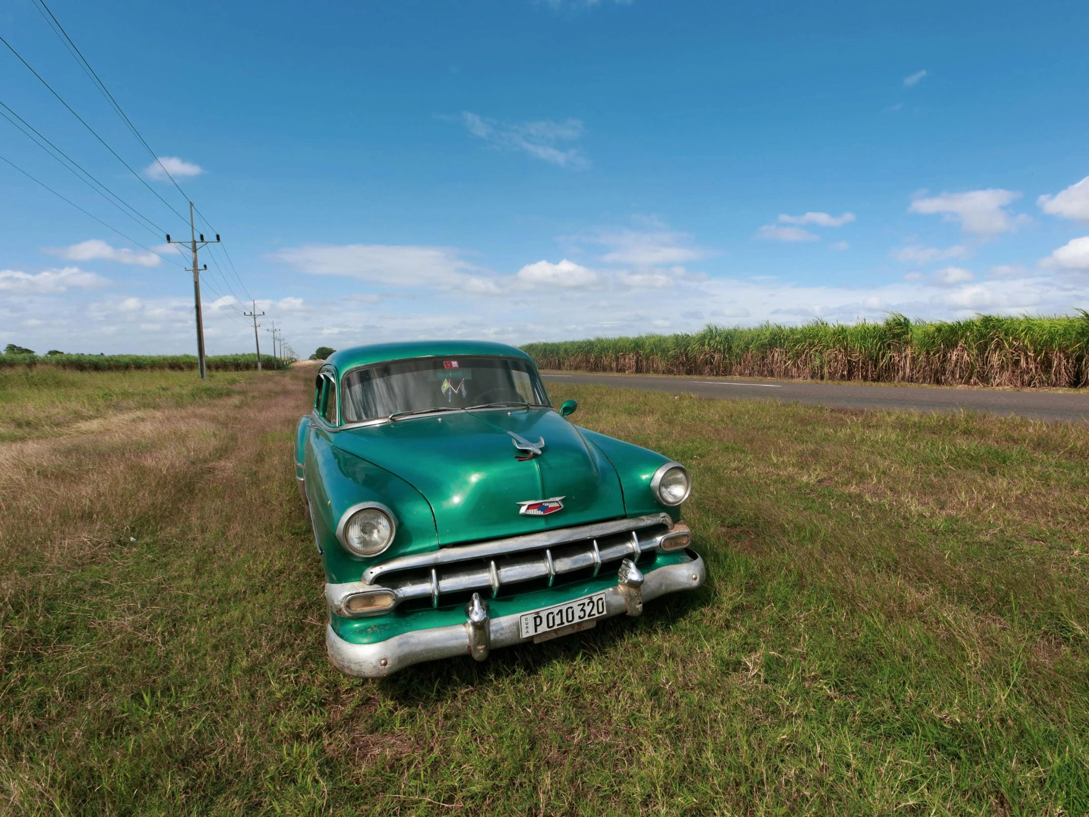 an old rusty green car sits in the middle of a cornfield