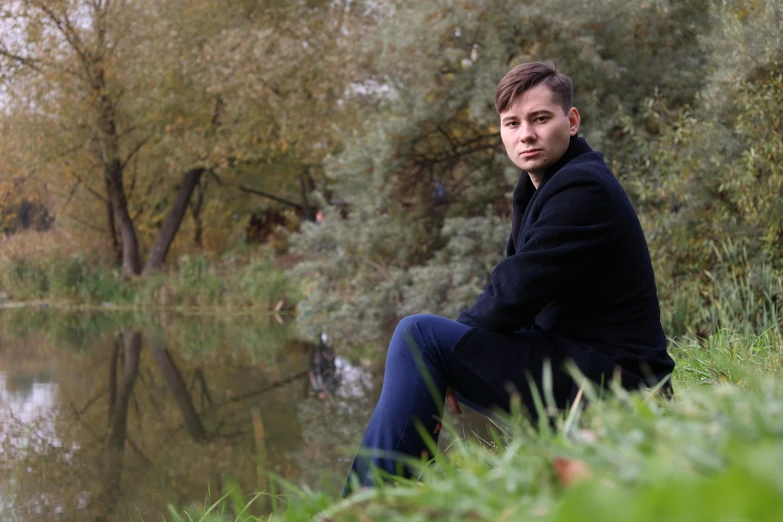 a young man sitting in front of water wearing a sweater