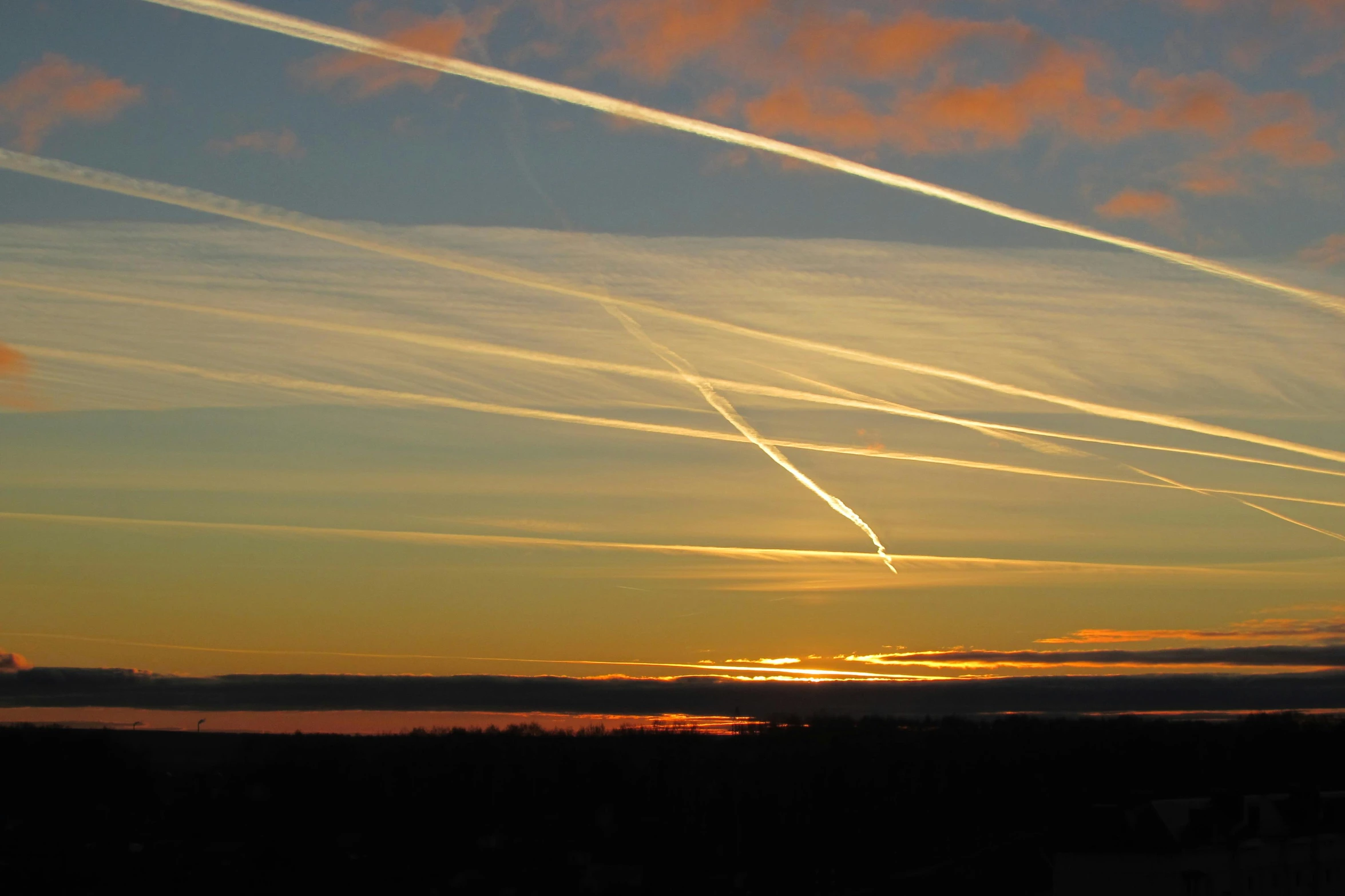 a beautiful sunset, with contrails over water and a building