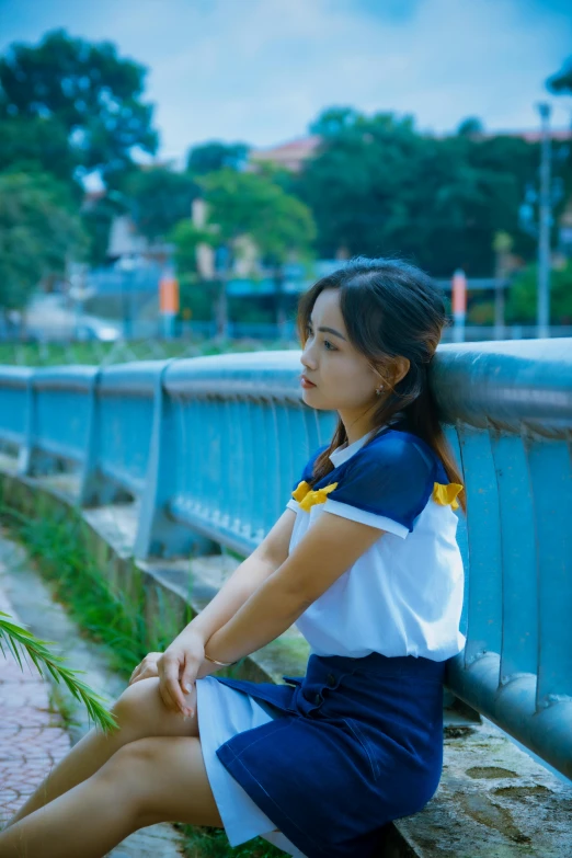 a girl sitting on the side of a fence in a blue and white dress