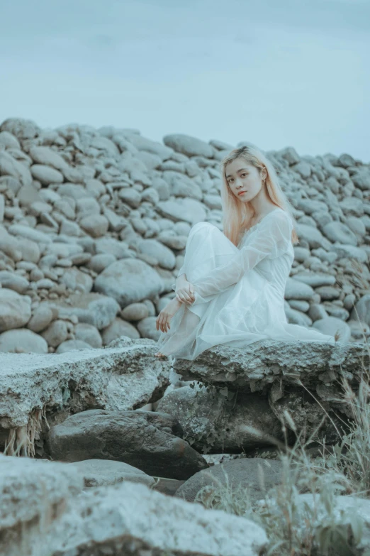 a woman in white sitting on rocks with her legs crossed