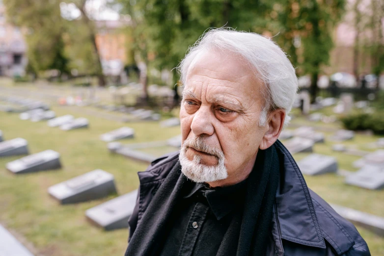 an elderly man wearing a black coat is standing near graves