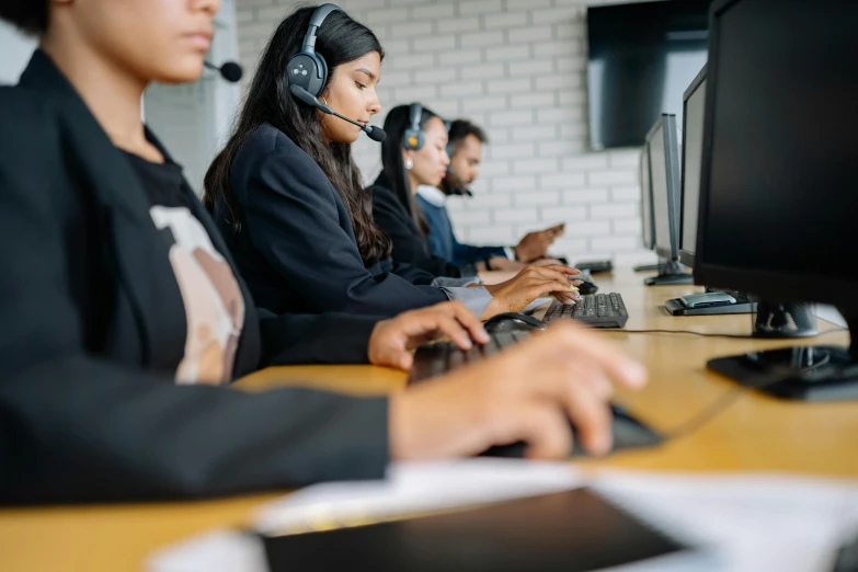 five people sitting in front of computers with headphones on