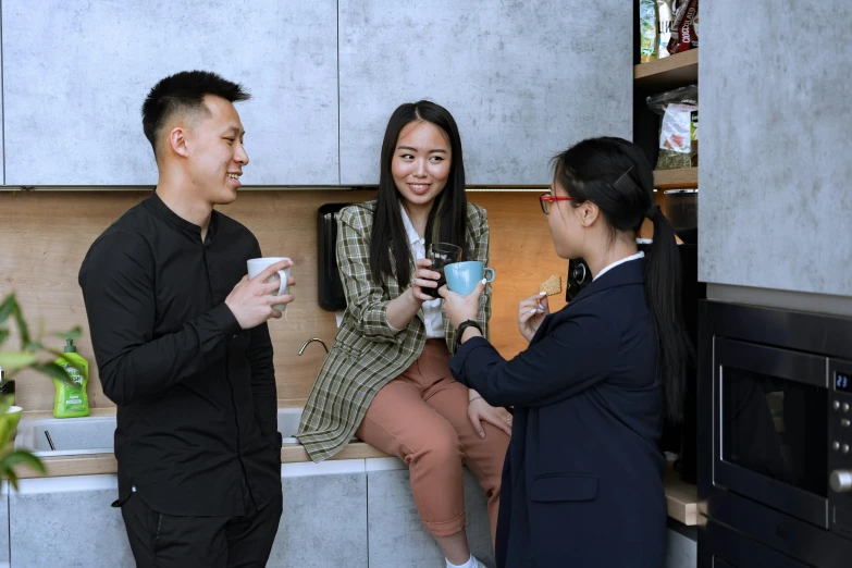 three asian people sitting in a kitchen on a counter having a conversation