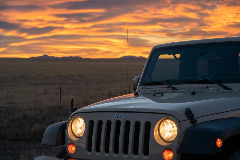 a jeep with the headlights on at sunset