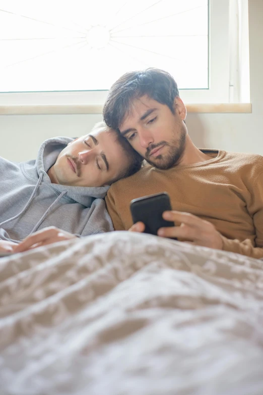 two guys are lying on their bed looking at a cell phone