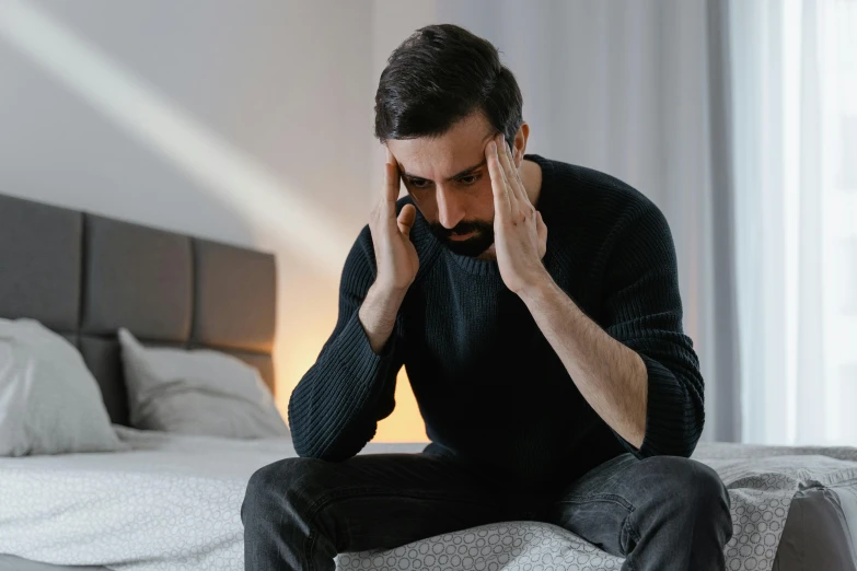 a man sitting on a bed holding his hands to his temples