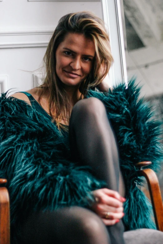 a woman sitting in a chair wearing a large green fur coat