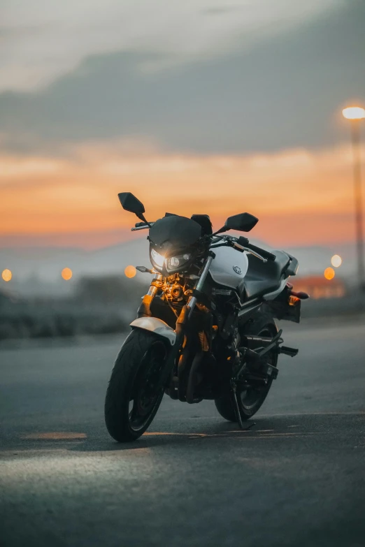 a motorcycle parked on a road with the sun setting in the background