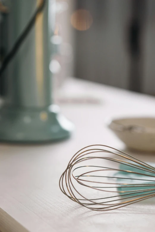 four metal whisks on a counter near a cup