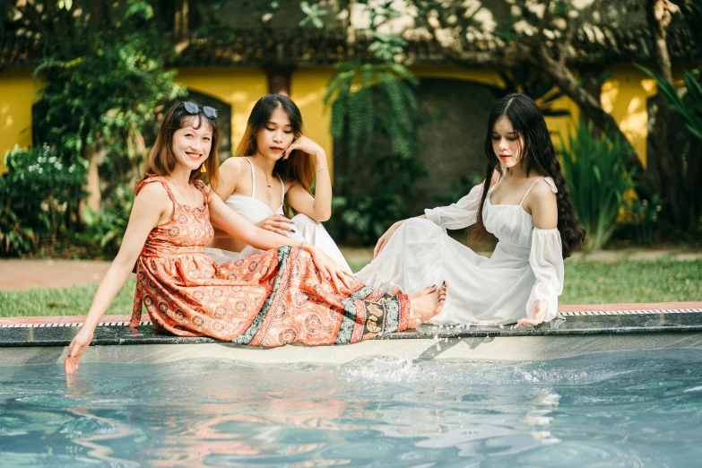 three pretty women sitting by a pool talking on cell phones