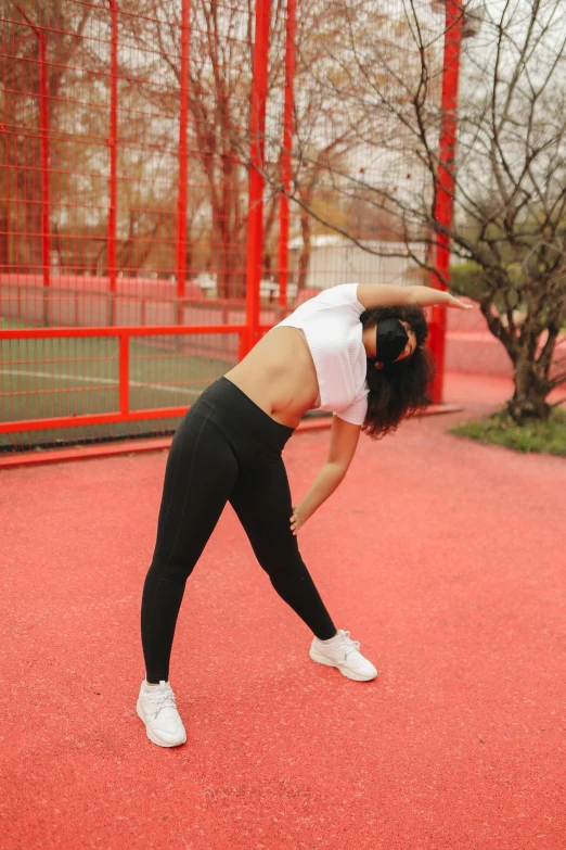 a woman stretching out in the park while wearing white sneakers