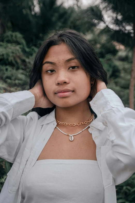 a woman in white shirt and gold necklace posing for a po