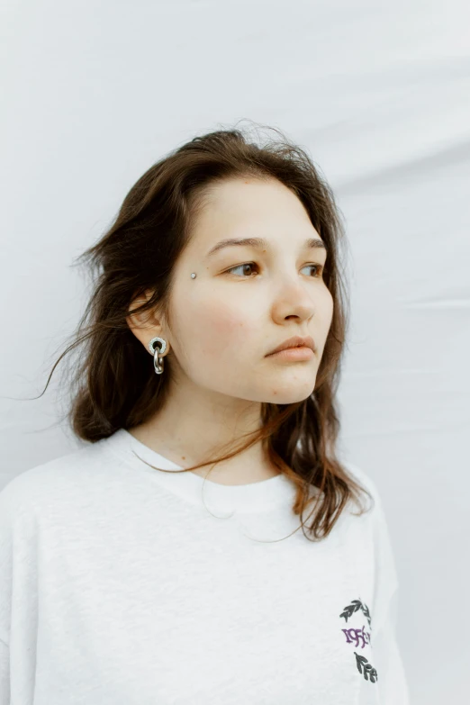 a girl wearing ear rings is standing near a wall
