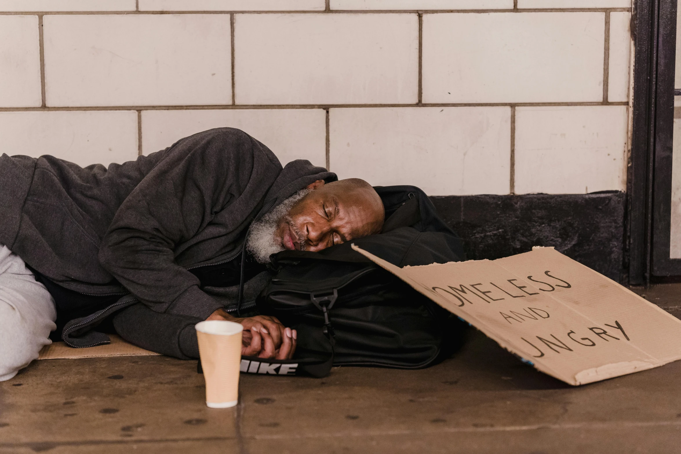 an old man sitting on the ground with a cardboard sign