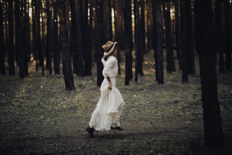 the woman is walking through the woods in a hat