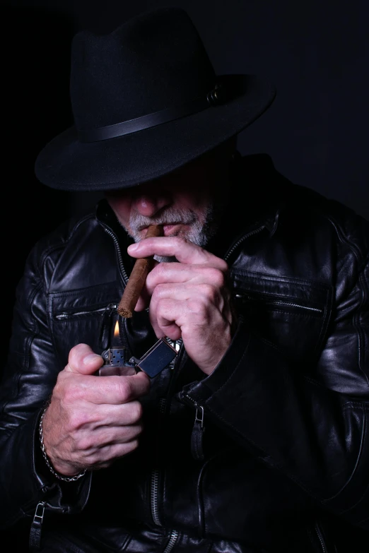 man in leather jacket and fedora lighting a cigar