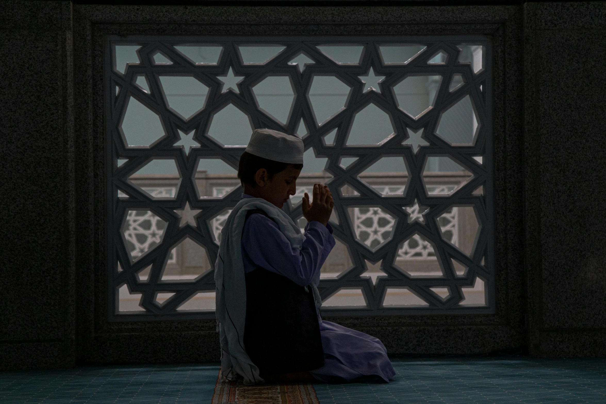 a young man in traditional dress sits on a rug and claps to music