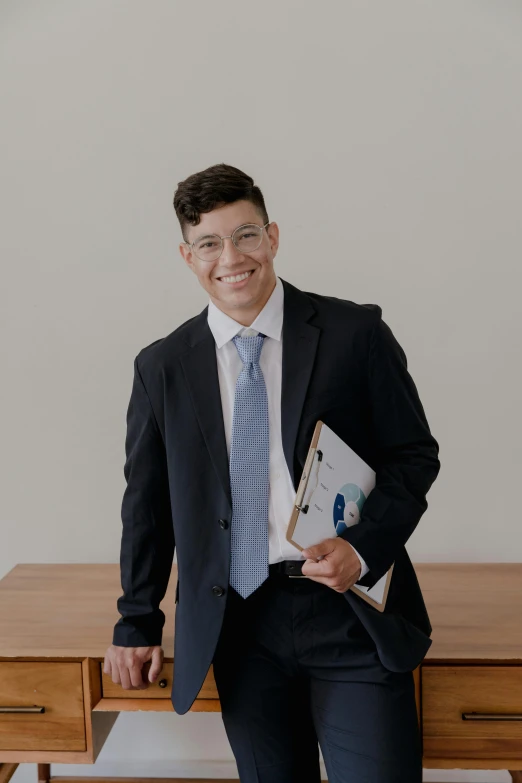 the man is holding two folders next to a wooden dresser