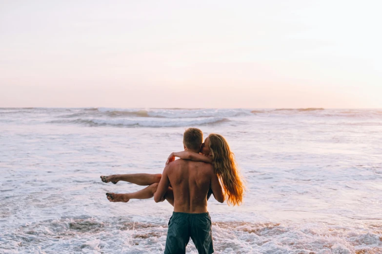 a man carrying a woman on his back, while she wades in the ocean