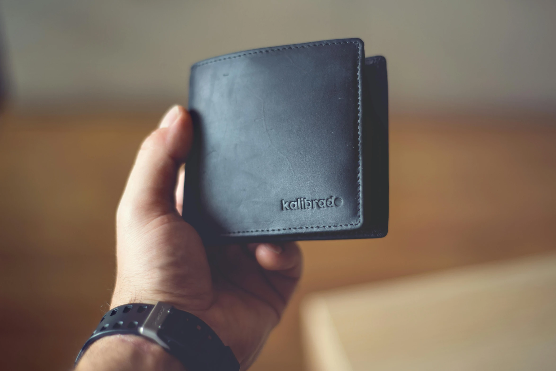 hand holding a small black wallet over a wooden table