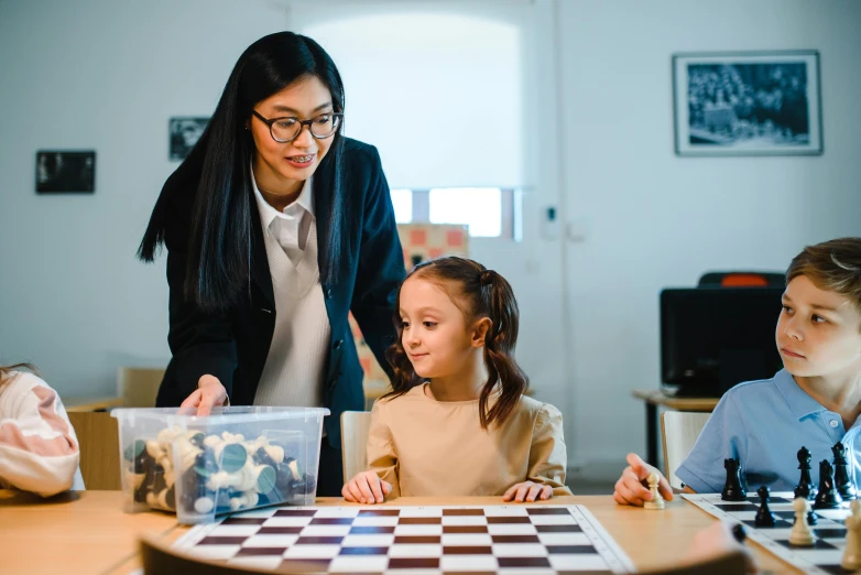 two girls playing chess at the school with a teacher