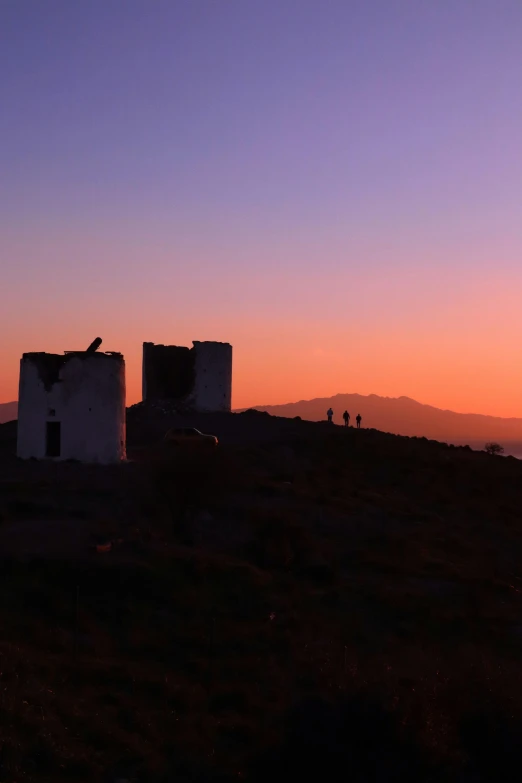 two stone building sit on top of the hill during the sunset