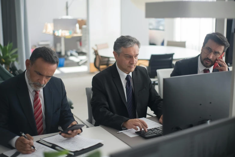 three business people sitting at a table working on computers