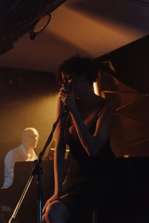 the woman sings into the microphone on stage with a man standing behind her