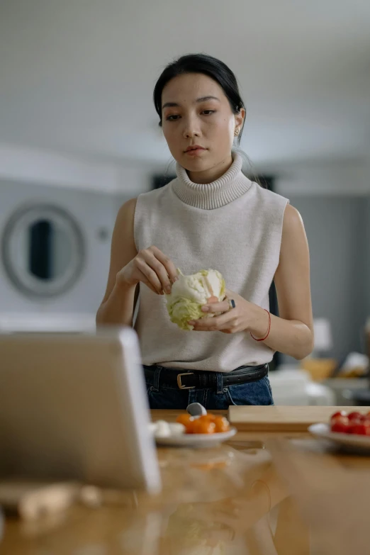 an asian woman is eating cabbage while working on her laptop