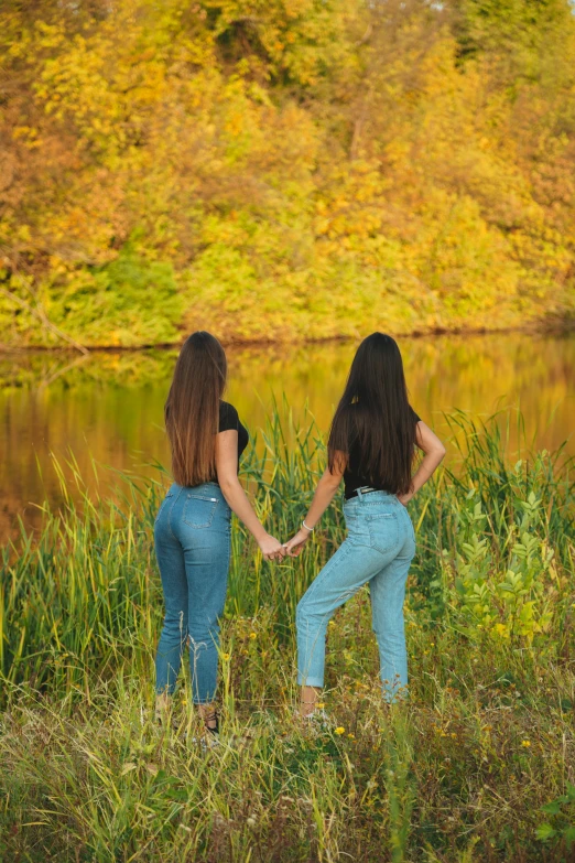 two women holding hands in a field near water