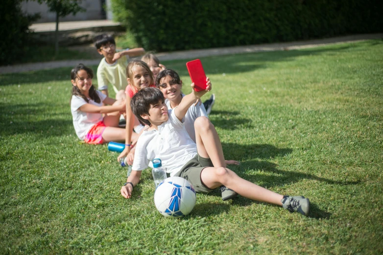 several s and one adult sitting on the grass with a soccer ball