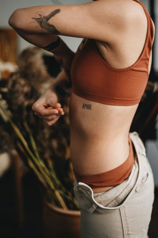 a woman with tattoos stands near a plant