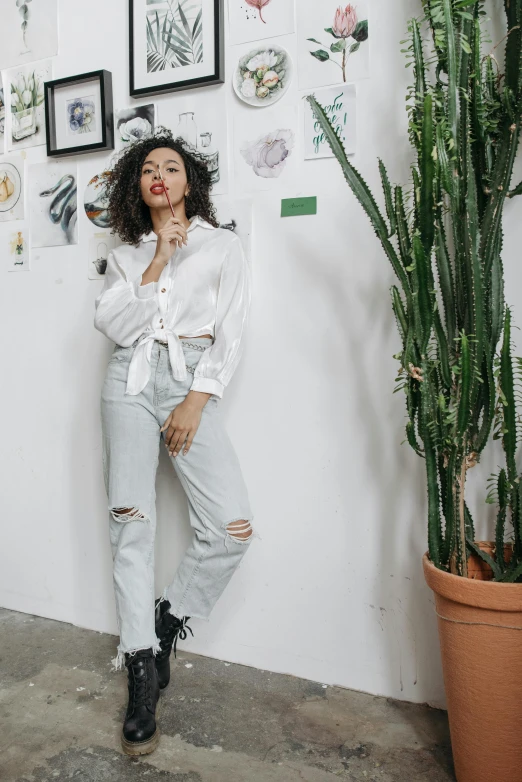 a woman wearing ripped jeans stands in front of a potted plant