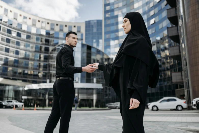 a man and woman dressed in black stand outside of an office building with a face covering