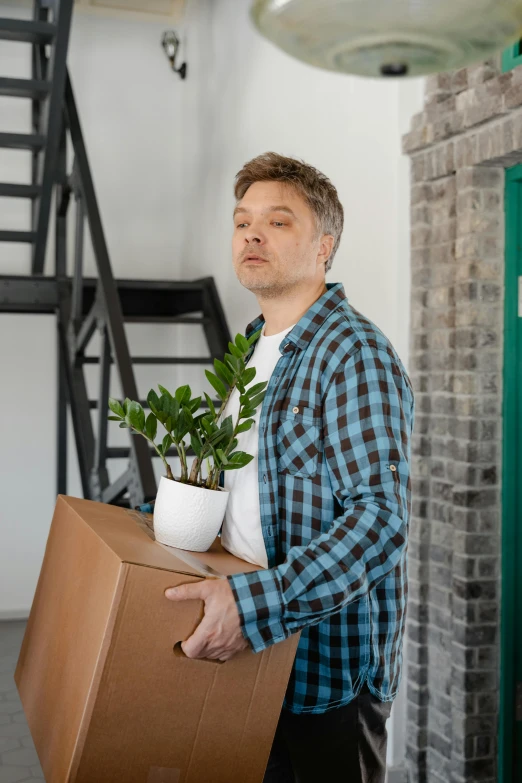 man carrying cardboard box and plants inside a building