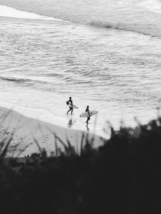 two surfers are walking on the shore line