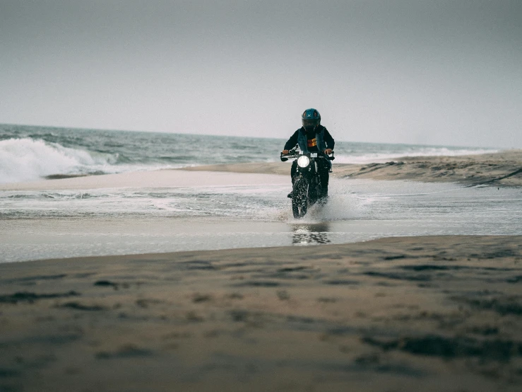 man riding a motorcycle on the beach, in the ocean