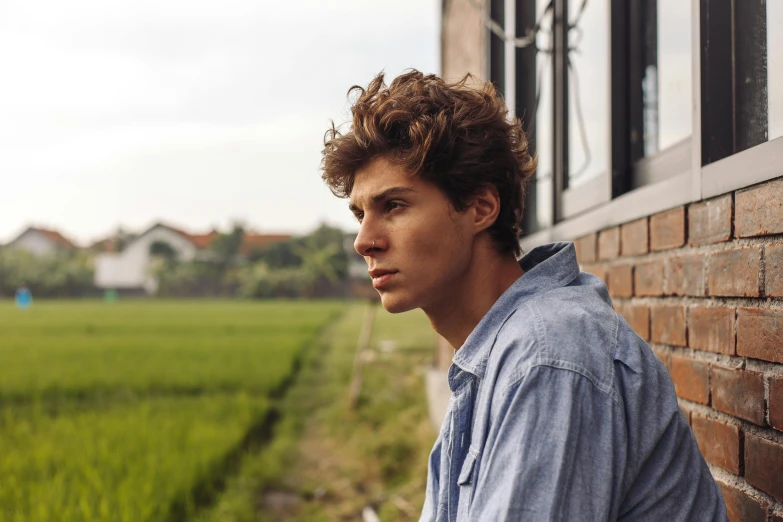 a young man is leaning against the side of the building