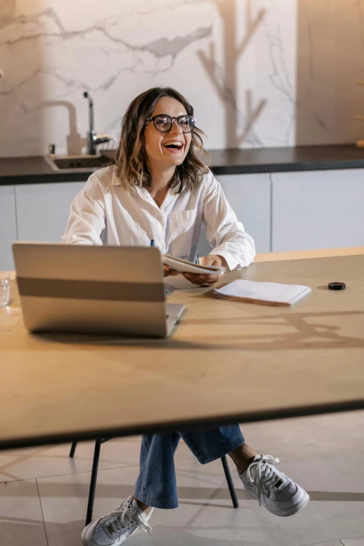 a smiling woman with eyeglasses sits in front of a computer