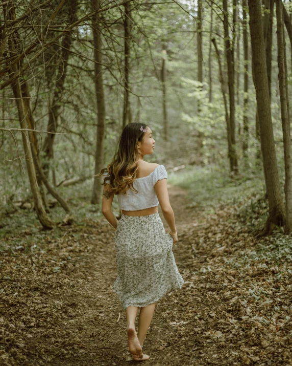 a beautiful woman in a skirt and shirt walking through a forest