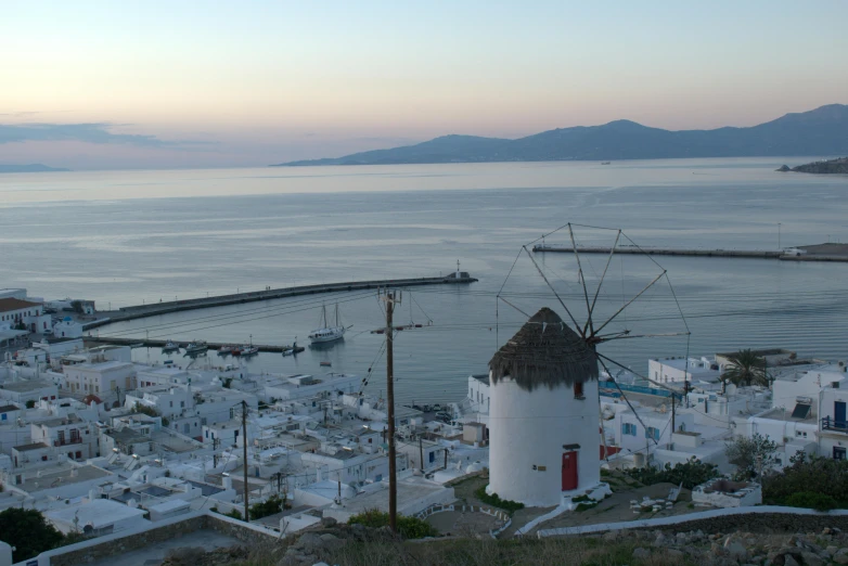 a windmill is sitting by the water at dusk