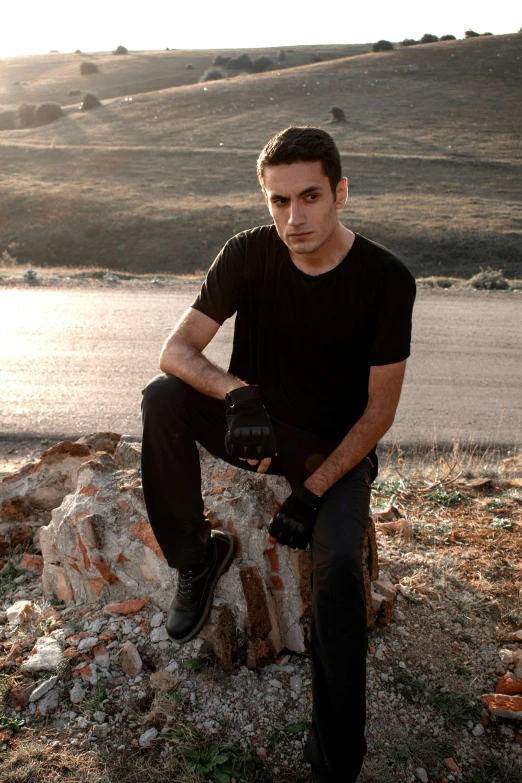 a young man with his hands on his knees sitting on a rock