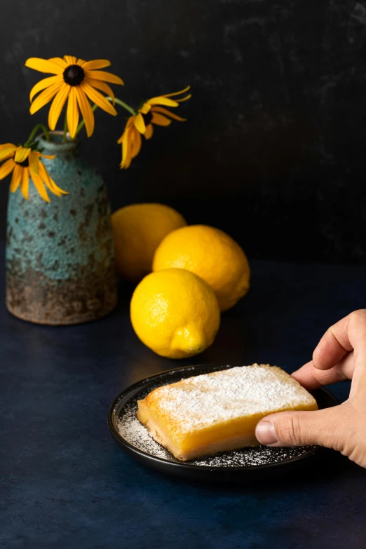 a hand touches a slice of toast on a plate with yellow flowers and lemons