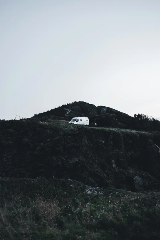 a white van sits atop a hill with a small stream