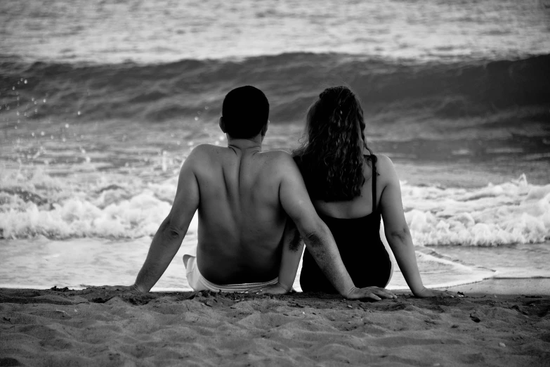 a man and woman sitting on top of a sandy beach