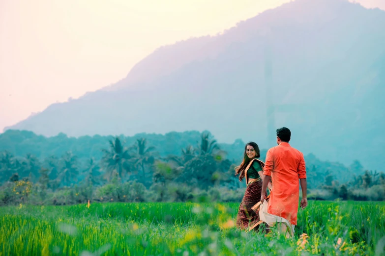 two women walk through the grass together near a hill