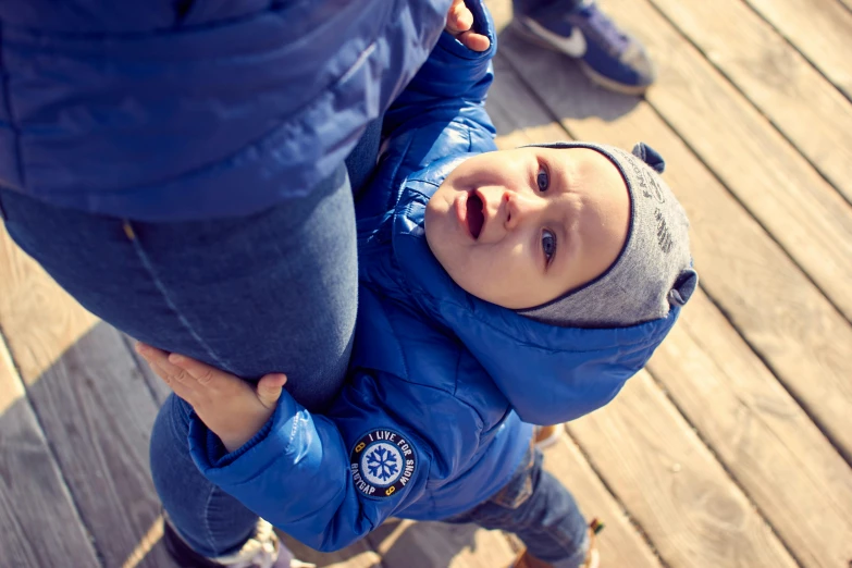 a baby in a blue jacket playing on a wooden floor