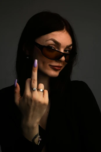 a woman in glasses, wearing a ring, is pointing her finger towards the camera